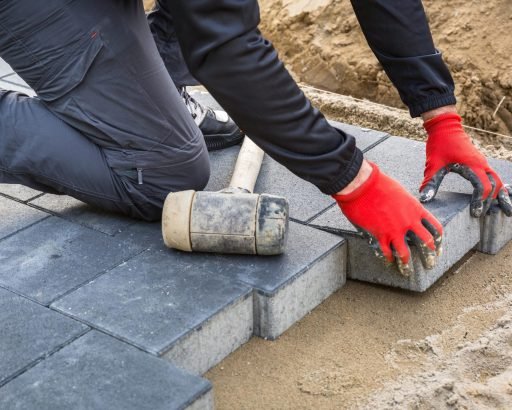 Hands of worker installing concrete paver blocks with rubber hammer